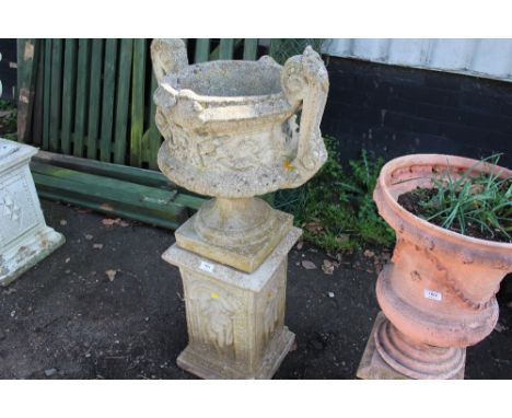 A concrete twin handled planter raised on decorative plinths