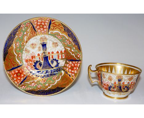 An English cup and saucer decorated in Japan palette with stylised urns before a fence, alternately panelled with stylised fl