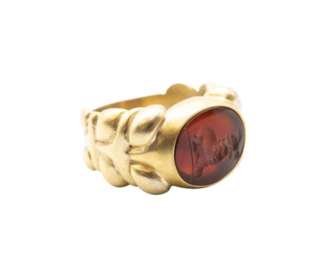 A CARNELIAN SIGNET RINGThe oval carnelian plaque featuring a carved intaglio of a seated griffin, to a heavy sculptural ring 