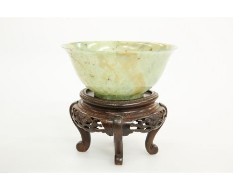 A CHINESE MOTTLED JADE BOWL, with everted rim, in grey/green stone with dark flecks, on a fret-carved wooden stand. Bowl 12.5