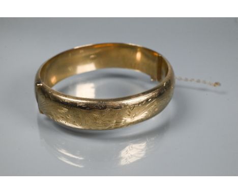 A 9ct yellow gold oval half hinged bangle, with foliate engraved decoration to front, concealed clasp and safety chain attach