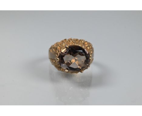 A 1970s style cocktail ring set with oval smokey quartz, claw set above high carved shoulders, 9ct yellow gold, size 0, appro