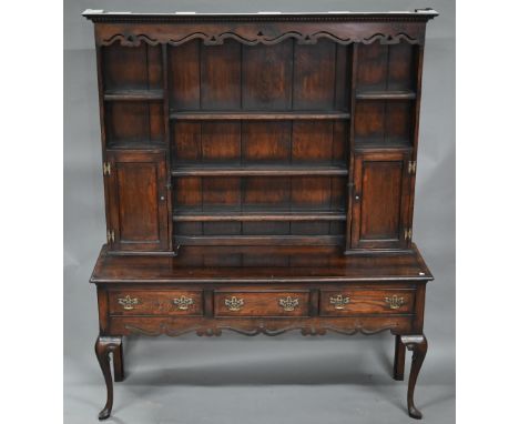 An 18th century style oak high dresser, the rack with dentil moulted canopy centred by open shelves flanked by cupboards, ove