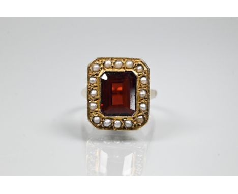 A yellow metal ring of rectangular design featuring emerald-cut red stone, probably garnet, surrounded by half pearls, stampe