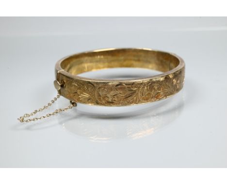 A silver-gilt half-hinged oval bangle with foliate engraved decoration, and safety chain attached, approx 19.3g  