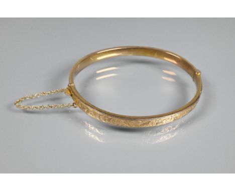 A 9ct yellow gold half hinged oval bangle, with engraved scroll decoration to one side, safety chain attached, approx 7.1 g  