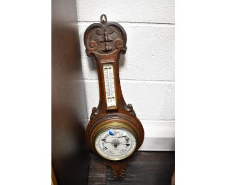 An early 20th century carved oak aneroid barometer, of wheel or banjo form, carved with scroll and bell flower elements, havi