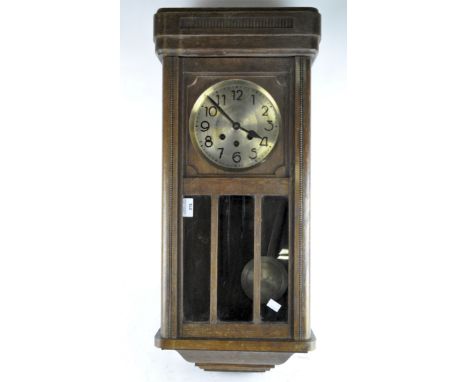 A 20th century wall clock, brass dial with Arabic numerals, the wooden case with carved details and a glass panel displaying 
