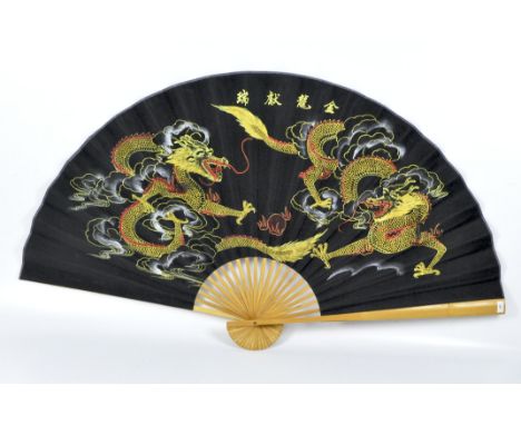 A large contemporary folding fan, wooden guards and stick with a fabric leaf decorated with dragons, length of guard 90cm