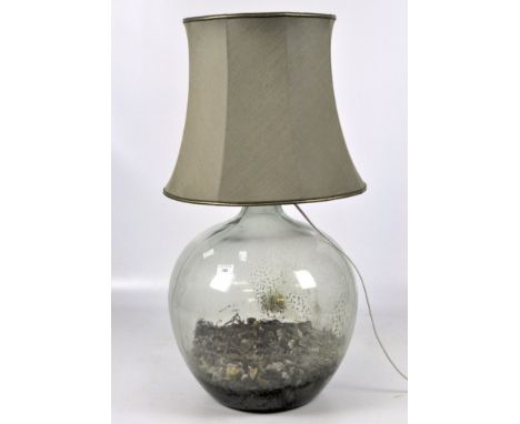 A large glass spherical bottle partially filled with rocks, converted into a contemporary electric lamp, with a green shade, 