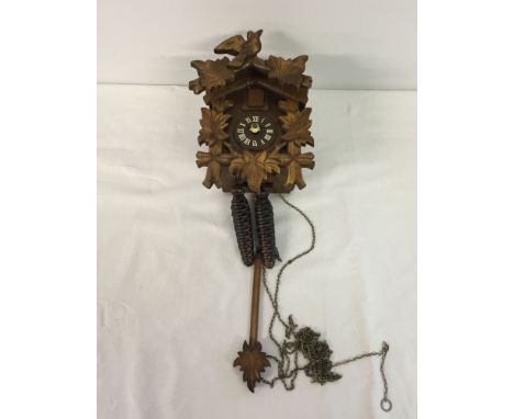 A carved wooden cuckoo clock with pendulum. Hands in need of repair.