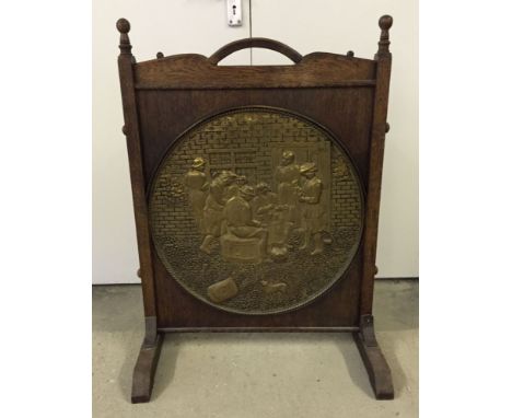 A large vintage wooden firescreen with central brass roundel depicting a tavern scene. Screen measures 63cm wide and 88cm tal