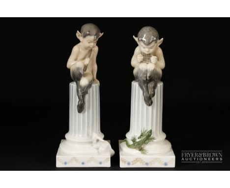 Christian Thomsen for Royal Copenhagen - a pair of figures of fauns sitting atop a truncated column playing pipes, one with a