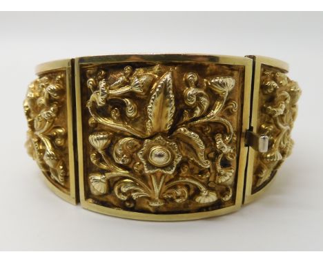 A gilded white metal repousse bangle, with scenes of flowers and fruit. Width at widest point 3.5cm, inner diameter approx 6c