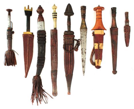 NINE VARIOUS NORTH AFRICAN TRIBAL KNIVES, eight with characteristic tooled leather scabbards, one with no scabbard, each with