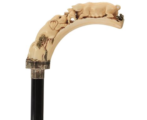 AN EARLY 20TH CENTURY WALKING CANE, the associated curved ivory handle carved as a family of pigs and piglets, with glass eye