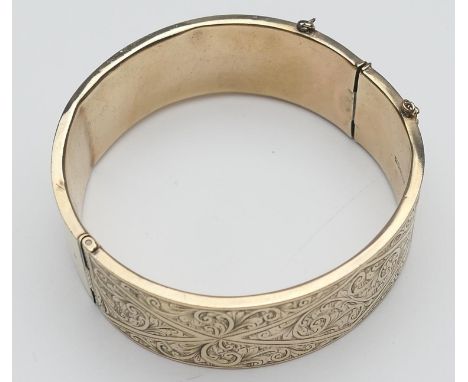 9ct gold hinged bangle, chased with foliate scrolls, with safety chain, interior size approx. 54mm, width 19mm, gross weight 