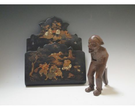 A Blackforest nutcracker carved as a man wearing a cap, and a papier mache wall rack decorated with Japanese Sumo and other f