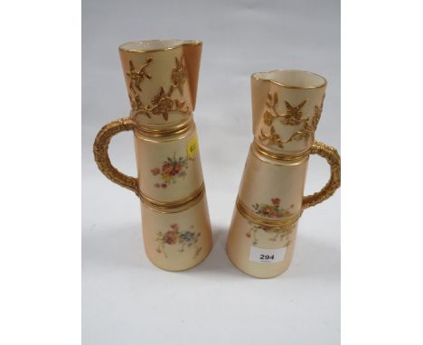 A pair of Royal Worcester blush ivory graduating jugs with gilded handles