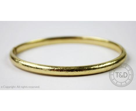 A yellow metal hinged bangle, stamped '585', with engraved scrolling foliate design and integral clasp, gross weight 11.4gms 