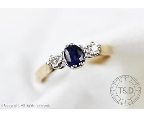 A diamond and sapphire three stone ring, the central oval sapphire flanked by two brilliant cut diamonds, each claw set in wh