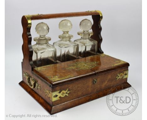A Victorian oak tantalus, with three cut glass decanters and stoppers and brass strapwork detailing, 28cm H x 36.5cm W x 26cm