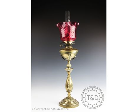 A Victorian cast brass oil lamp, with cranberry glass shade on a baluster column cast with acanthus leaves, 81cm