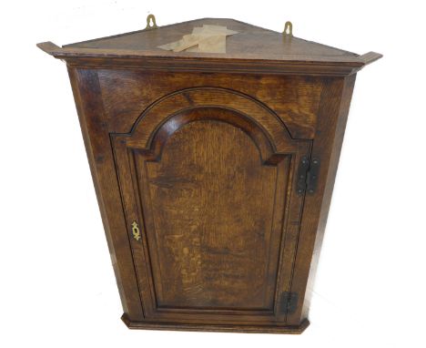 A mid 18th century style (good later reproduction) hanging oak corner cupboard: single arch-topped fielded panel door with H-