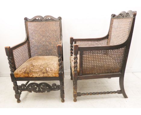 A pair of large and unusual heavy stained wood and rattan caned bergère chairs: each with carved scrolling top rail above can