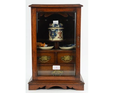 An early 20th century oak smokers cabinet with glazed door, enclosing a fitted interior, tobacco jar and two matching dishes,