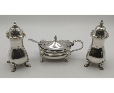 A silver three-piece cruet set by Goldsmiths and Silversmiths to include a mustard pot and salt and pepper pot with blue glas