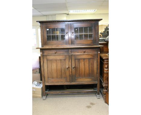 A large continental oak cabinet of Arts & Crafts design the raised top fitted with a pair of lead light glazed doors above dr