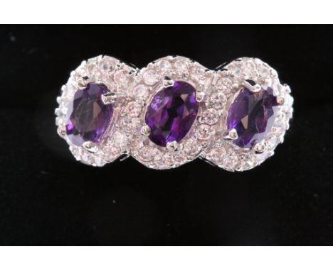 A ladies silver dress ring set with three amethyst coloured stones with white stone surround