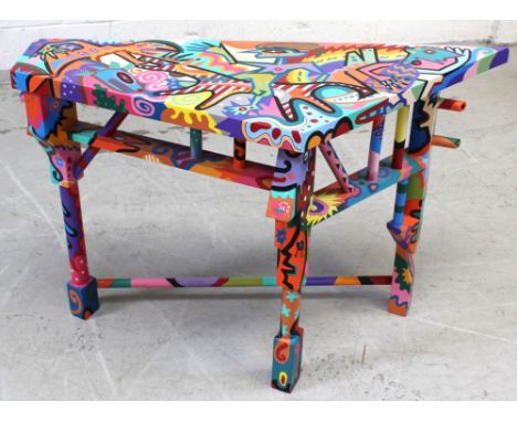 A side table with trapezoid-shaped top, hand-painted throughout with abstract figures and animals in an extensive palette, on