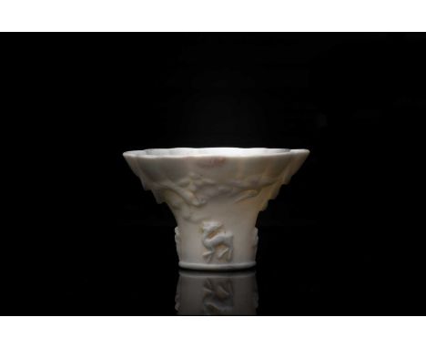 A Chinese blanc de Chine cup, 18th century, modelled as a rhinoceros horn libation cup with scalloped rim. with relief decora