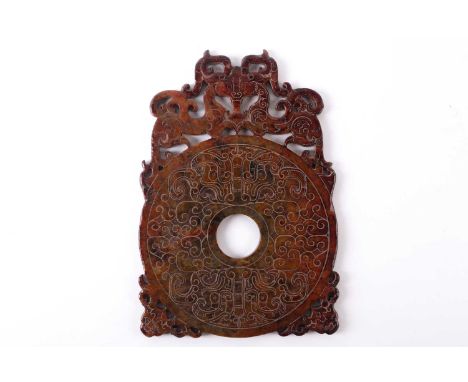 A Chinese carved and pierced variegated russet jade Bi disc of archaic form with stylized dragon mantle and engraved decorati