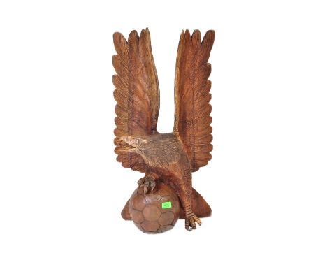 A vintage 20th century carved wooden sculpture of an eagle with upstretched wings resting on football. It measures approx. 78