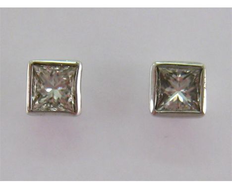 A pair of 18 carat white gold and single stone diamond earrings, the rub over set princess cut stones totalling approx. 1 car