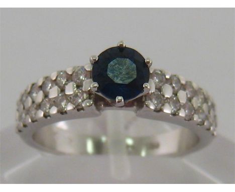 An 18 carat white gold, sapphire and diamond ring, the central round cut sapphire 5.2mm, to brilliant set shoulders, the shan