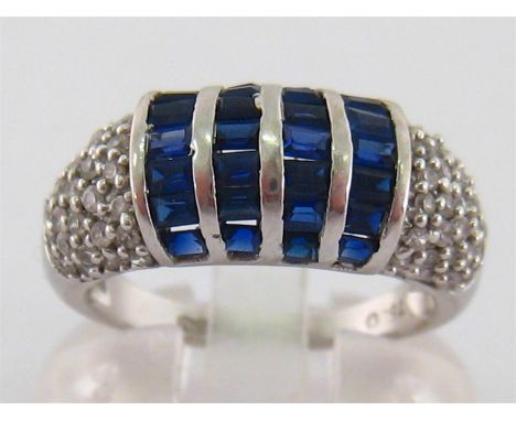 An 18 carat white gold, sapphire and white stone dress ring, set to the centre with four rows of calibre cut sapphires, to pa