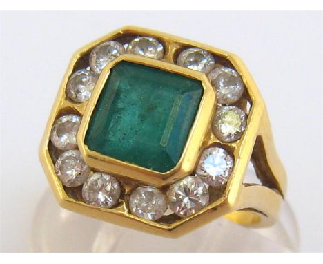 An 18 carat gold, emerald and diamond ring, the square cut stone 7.4 x 7.4 x 5.1 (deep) mm, in a surround of brilliants total