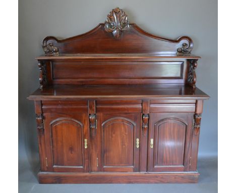 A mahogany sideboard, the shaped carved back with shelf, the lower section with three drawers above three cupboard doors rais