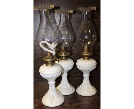 THREE WHITE CERAMIC BASED OIL LAMPS
all with burners, wicks and fluted rimmed glasses, each 43cm high
Note: Condition good
