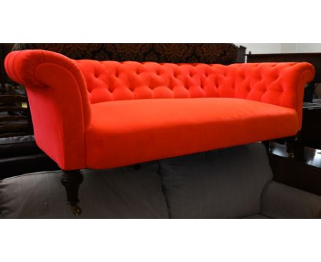 A Chesterfield two-seater sofa in neon vermillion button back upholstery on turned supports with brass casters, 170 cm wide x