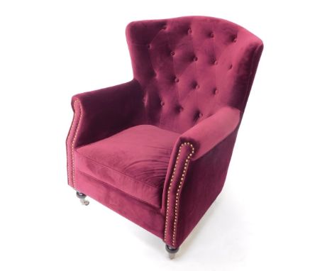 A wing back armchair, upholstered in purple button back velvet, raised on ebonised turned legs, on castors.