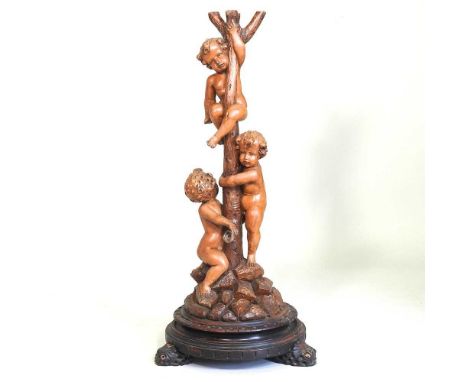An early 20th century Italian carved pine figural lamp base, decorated with three cherubs, climbing a tree trunk, on a natura