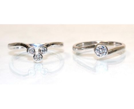 An 18 carat white gold solitaire diamond ring, a round brilliant cut diamond in a rubbed over setting, to bypass scroll shoul