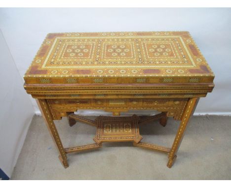 An early 20th century bone/ivory and mixed veneered marquetry games table, with a rotating foldover top, enclosing a double, 