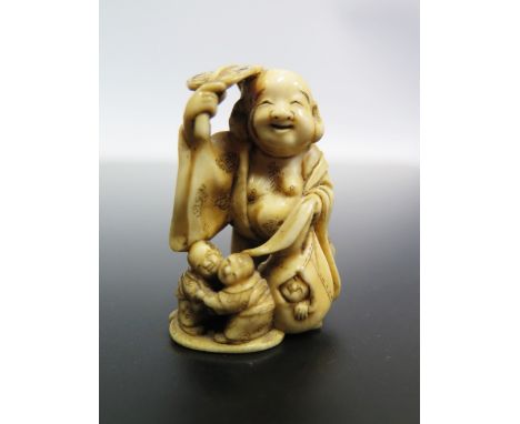A Japanese Meji Period Carved Ivory Netsuke in the form of laughing Buddha with children at feet