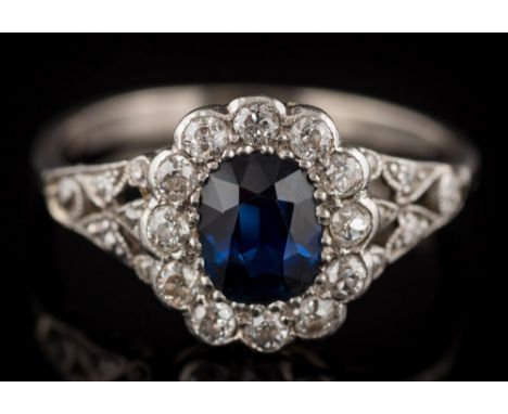 A sapphire and diamond oval cluster ring: the oval sapphire approximately 6mm long x 4.8mm wide x 2.7mm deep, within a surrou